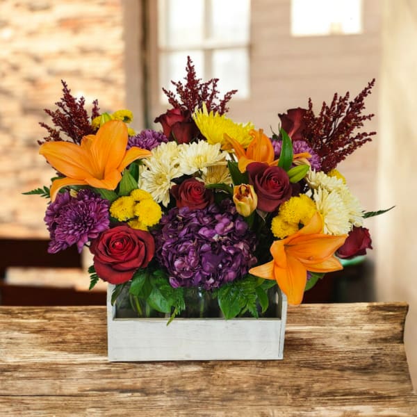 Mixed bouquet in a white wooden box with orange lilies, red roses, and purple hydrangea