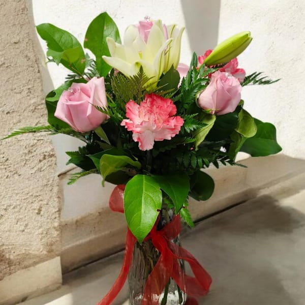 Pink roses and a white lily in a glass vase with a red ribbon
