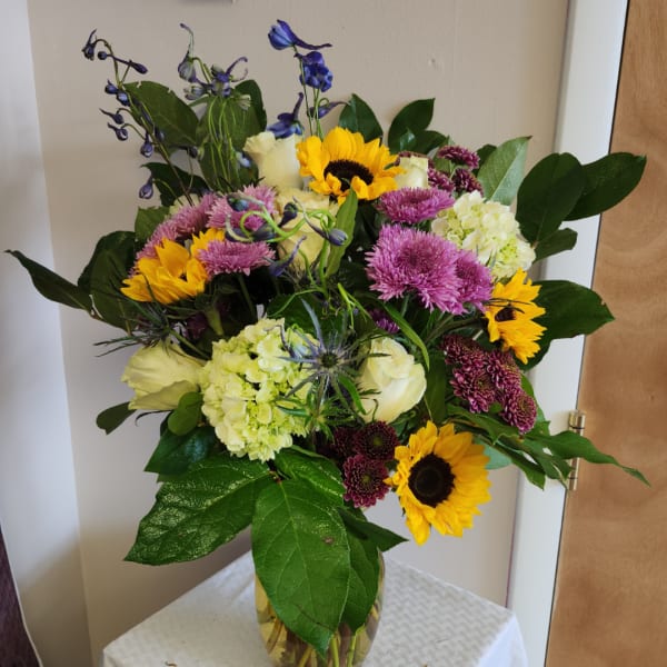 Mixed bouquet with sunflowers, white roses, purple blooms, and a glass vase