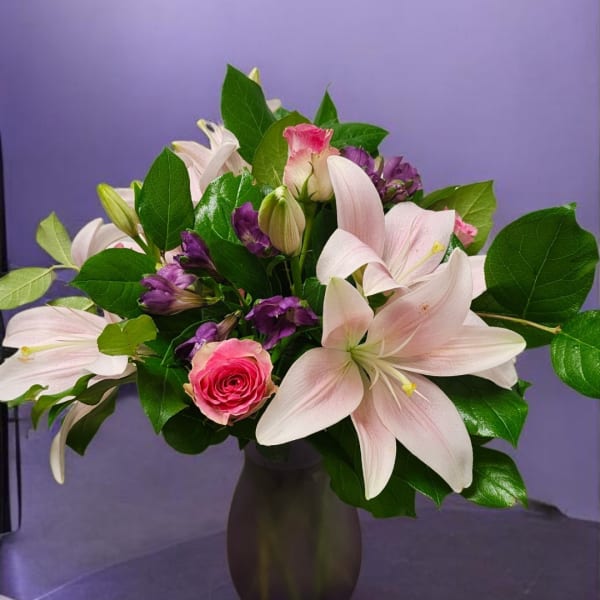 Pink lilies and roses in a dark vase with purple flowers