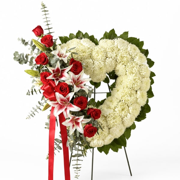Heart-shaped floral wreath with white chrysanthemums, red roses, and lilies on a stand