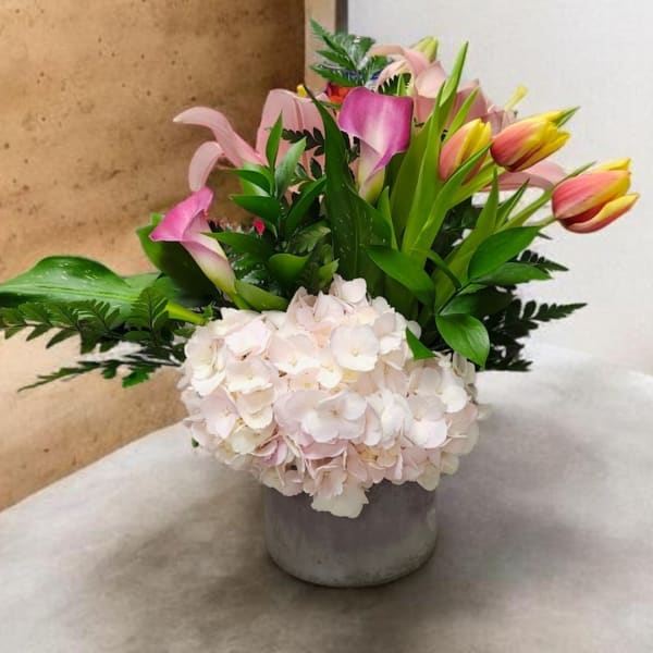 Pink calla lilies and tulips in a gray vase with pale hydrangeas