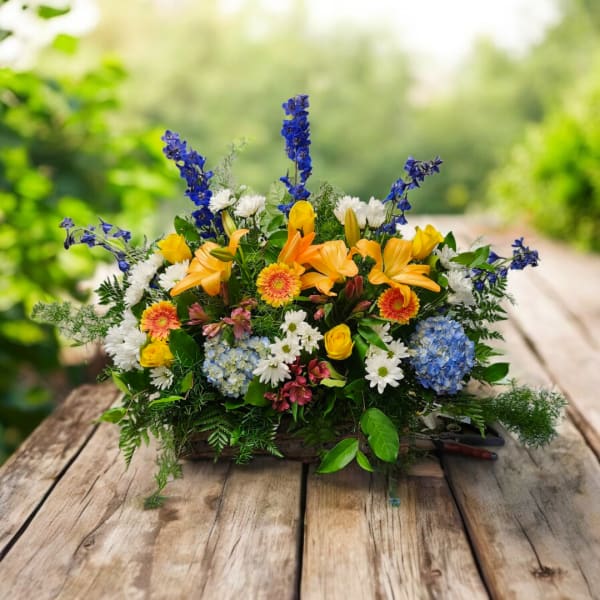Mixed bouquet with yellow lilies, blue delphinium, and white daisies in a low container