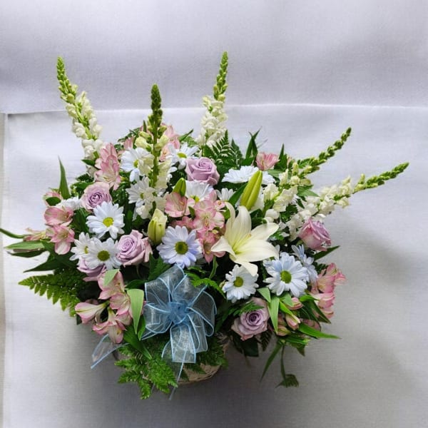 Pastel mixed flower arrangement with daisies, roses, lilies, and snapdragons in a basket