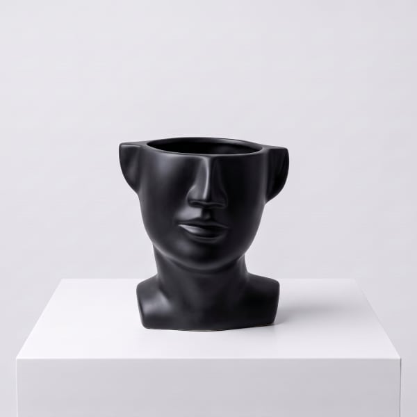 Black face-shaped vase on a white pedestal