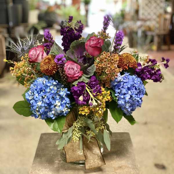 Colorful bouquet with blue hydrangeas, pink roses, and purple flowers in a glass vase