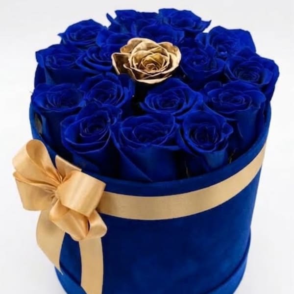 Blue roses arranged in a round box with a gold ribbon and one gold rose