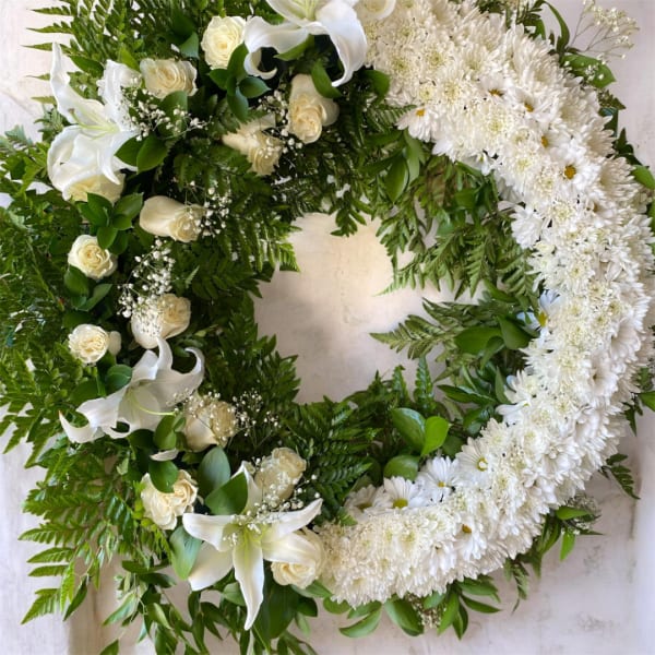 White floral wreath with lilies, roses, and daisies on a light background