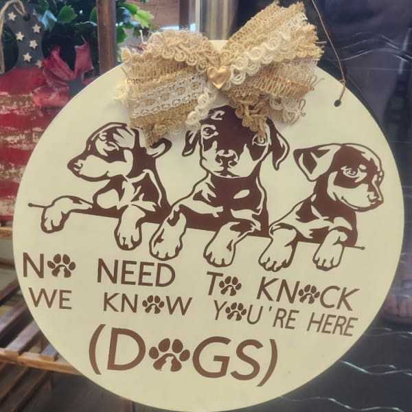 Round hanging sign with three puppy illustrations and the words "No need to knock, we're here (dogs)"