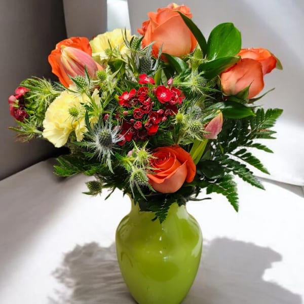 Orange roses and mixed flowers in a green vase