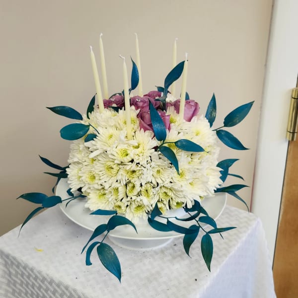 White chrysanthemum arrangement with purple roses and tall candles in a white bowl