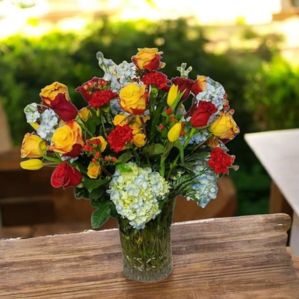 Bouquet of red and yellow roses with blue hydrangeas in a glass vase