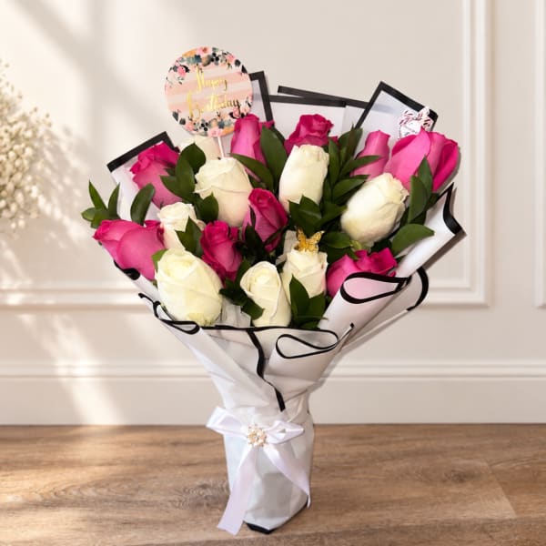 Bouquet of pink and white roses wrapped in white paper with a birthday topper