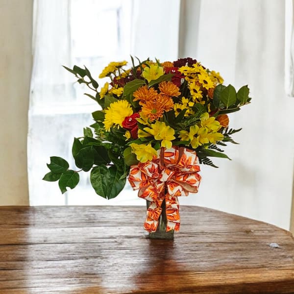 Bouquet of yellow and orange flowers in a glass vase with a patterned ribbon