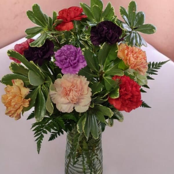 Mixed carnations in a clear glass vase with variegated greenery