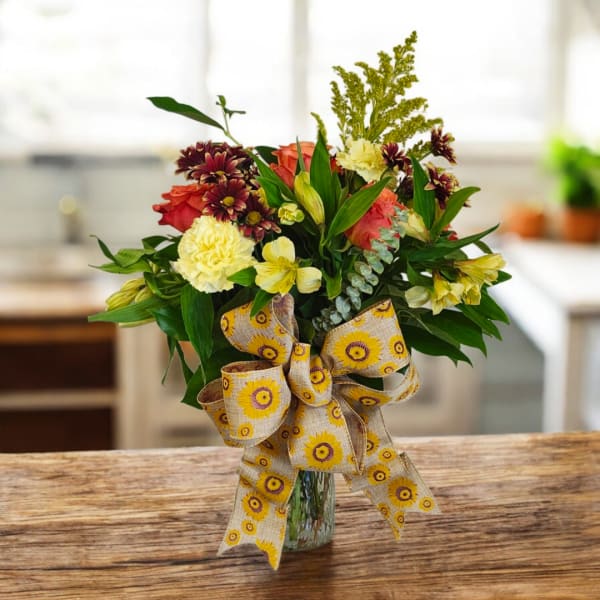 Mixed bouquet in a glass vase with a large patterned ribbon