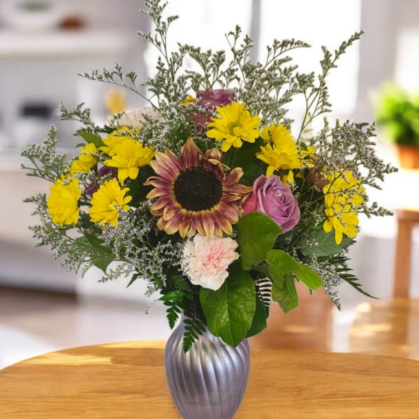 Mixed bouquet in a silver vase with a sunflower, yellow daisies, and pink roses