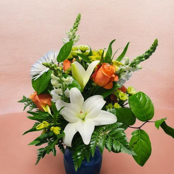 Mixed bouquet with white lilies, orange roses, and green filler in a blue vase