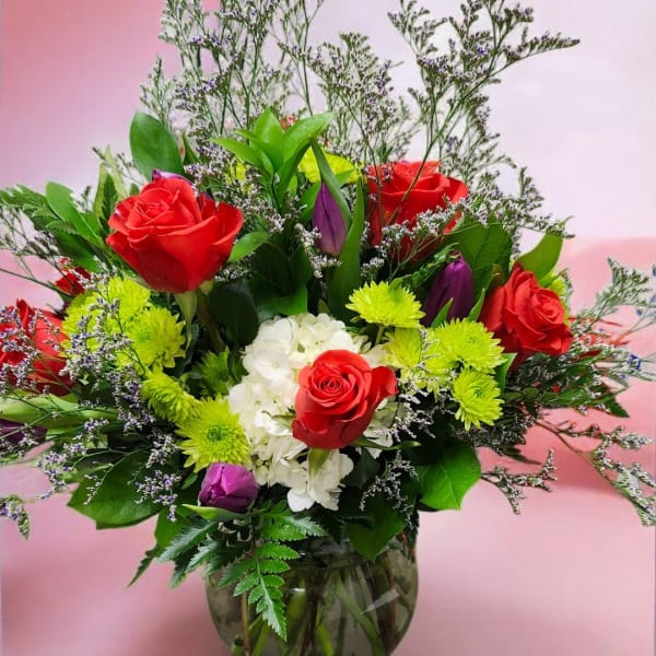 Red roses and white hydrangea in a glass vase with green and purple accents