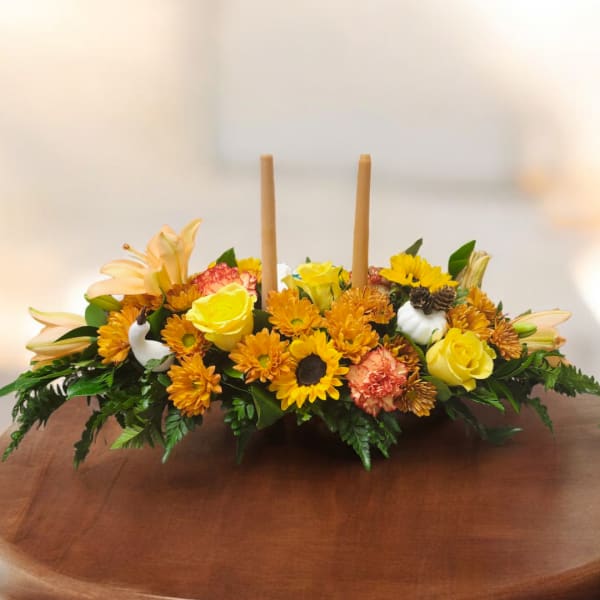 Low floral centerpiece with yellow roses, orange mums, and candles