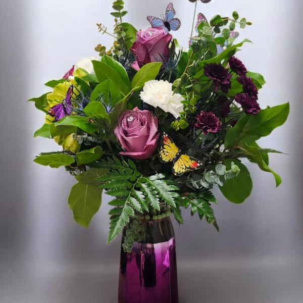 Bouquet of purple and white flowers in a purple vase with butterfly picks