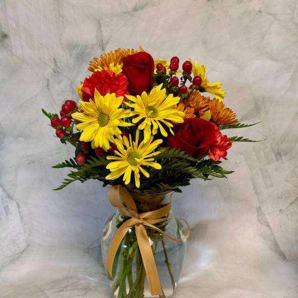 Bouquet of red roses and yellow daisies in a glass vase with a ribbon