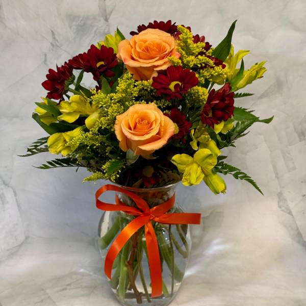 Bouquet of peach roses, red daisies, and yellow flowers in a glass vase