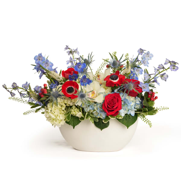 Mixed bouquet in a white bowl vase with red, blue, and white flowers