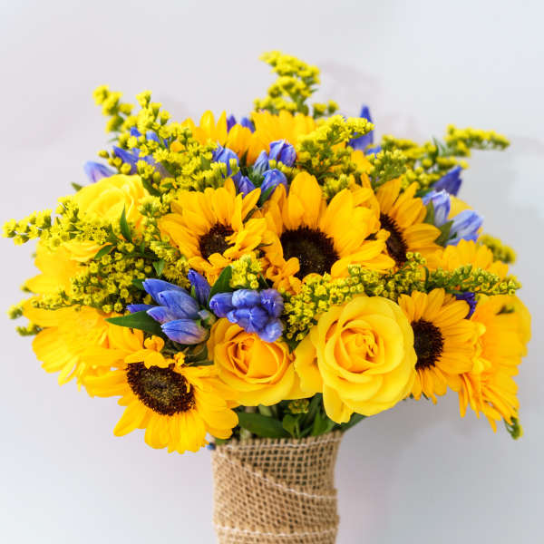 Bouquet of yellow sunflowers and roses with blue flowers wrapped in burlap