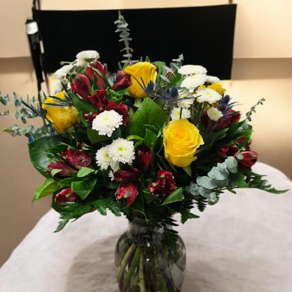 Bouquet of yellow roses, red alstroemeria, and white daisies in a glass vase
