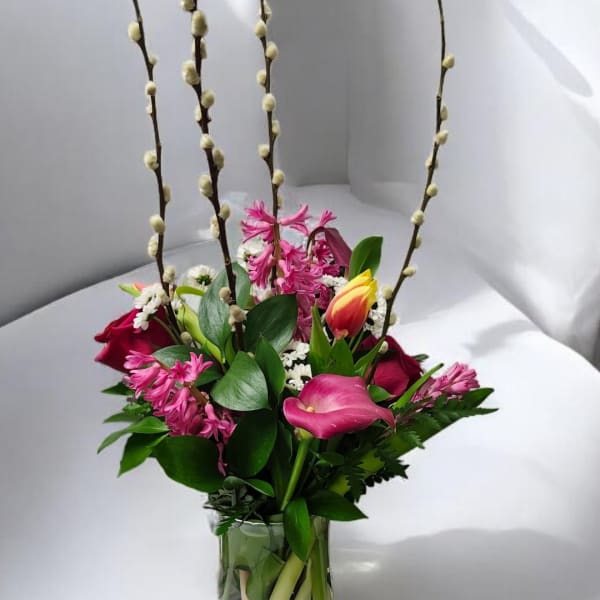 Pink and yellow mixed bouquet in a clear glass vase with tall pussy willow stems