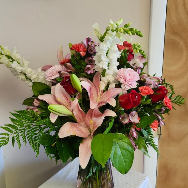 Mixed bouquet with pink lilies, red roses, and white snapdragons in a glass vase