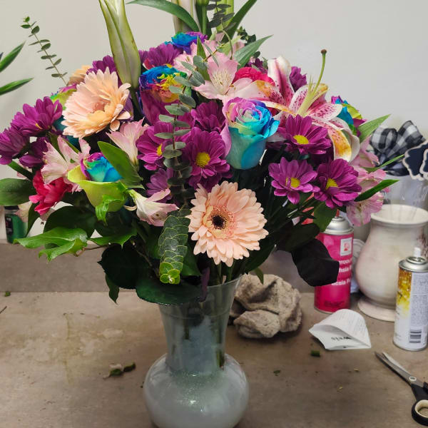 Mixed bouquet in a glass vase with purple daisies, lilies, and peach gerberas