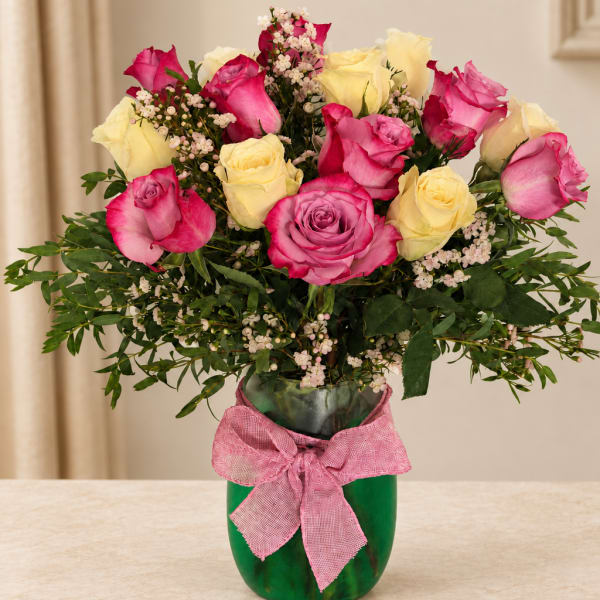 Pink and yellow roses in a green vase with a pink ribbon