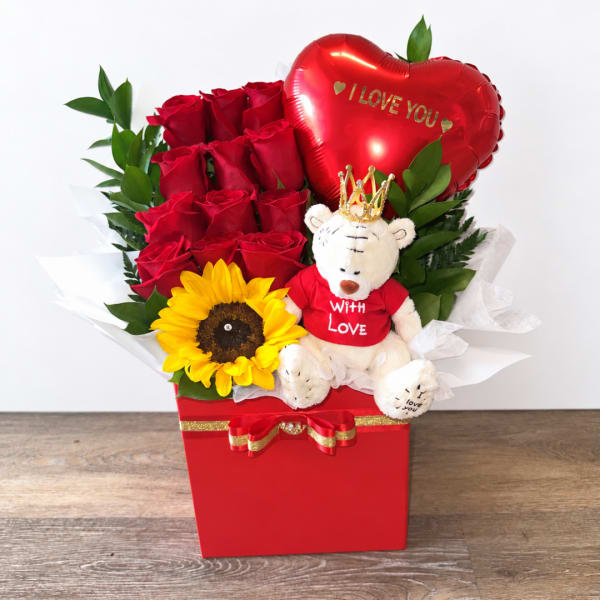 Red roses with a sunflower, teddy bear, and heart balloon in a red box