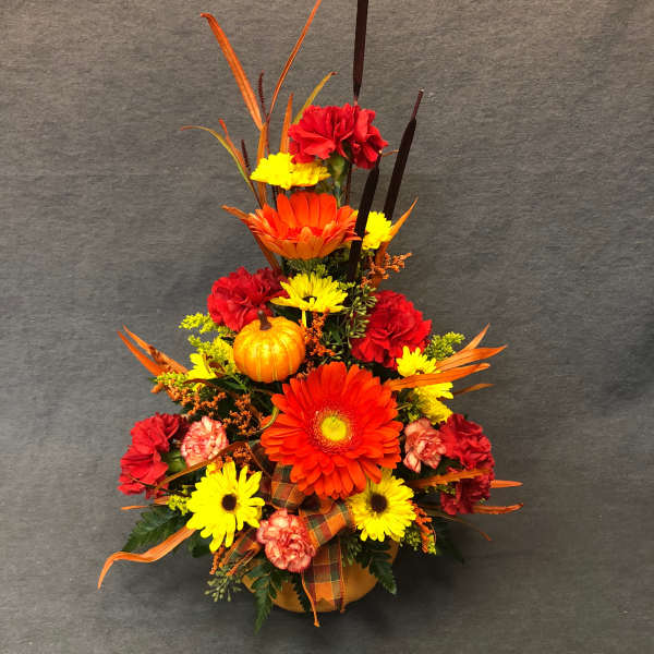 Autumn floral arrangement with gerbera daisies, carnations, and a small pumpkin in a vase