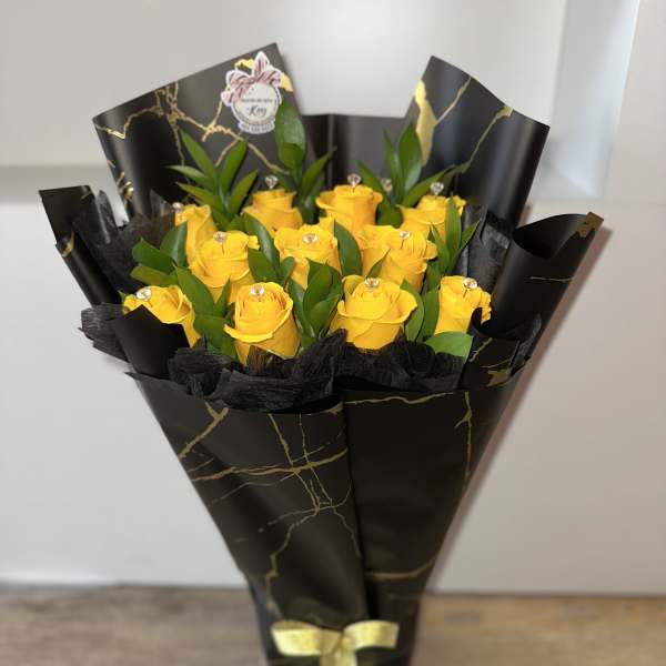 Bouquet of yellow roses wrapped in black paper with a gold ribbon