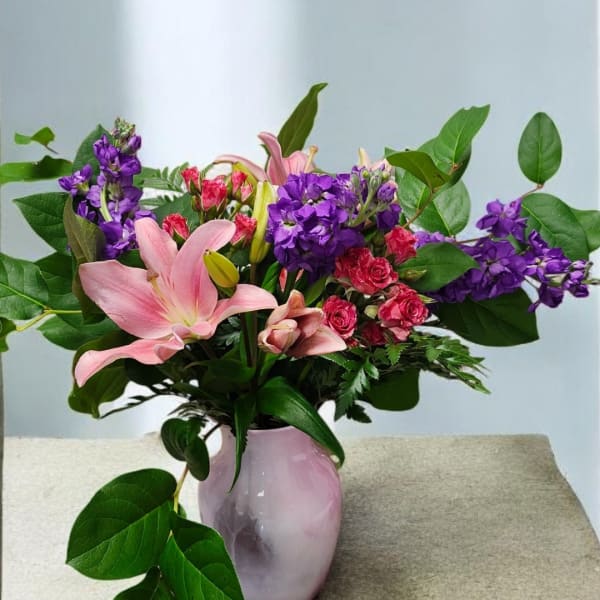 Pink lilies and purple flowers arranged in a pale vase