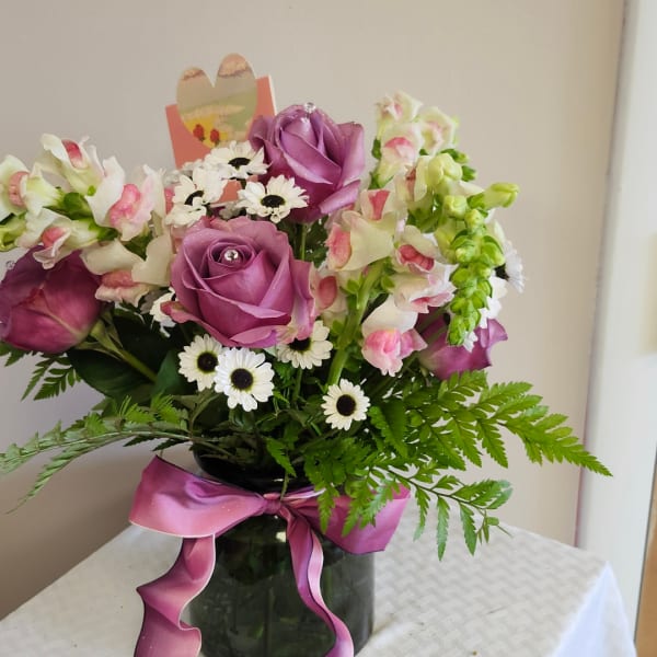 Pink and white flower arrangement in a dark vase with a purple ribbon