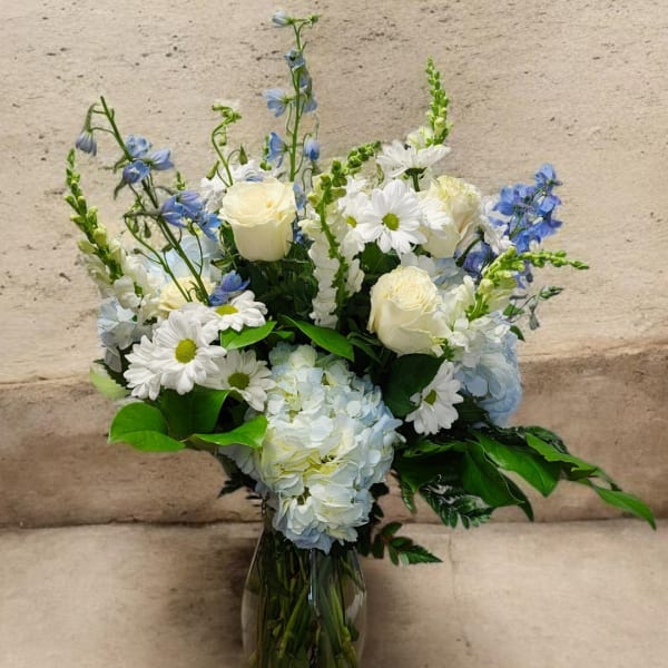 White roses, daisies, and blue flowers in a clear glass vase