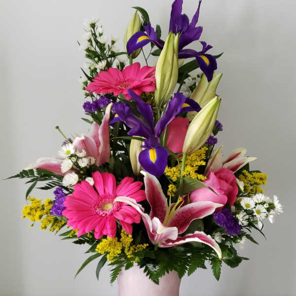 Mixed bouquet with pink gerberas, purple irises, and lilies in a pink vase
