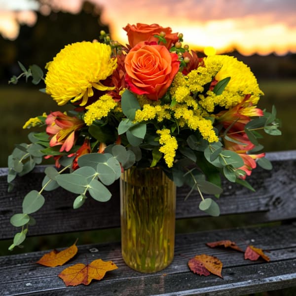 Orange and yellow flower arrangement in a tall glass vase