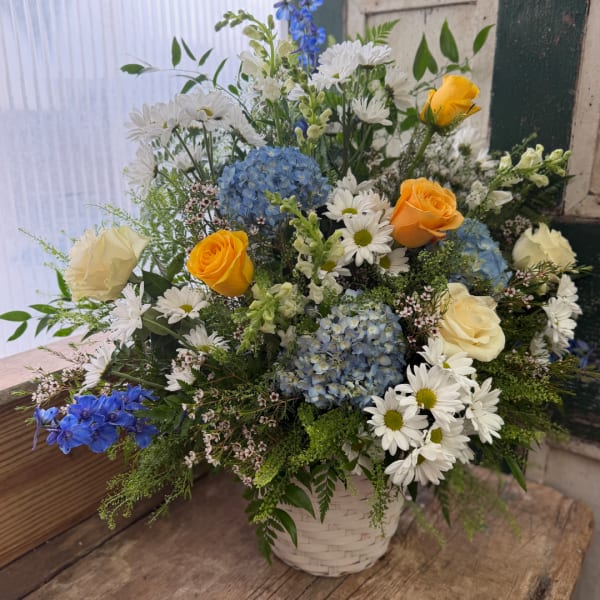 Mixed bouquet of blue hydrangeas, white daisies, and yellow roses in a basket
