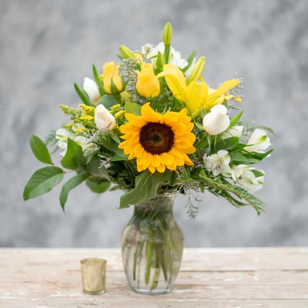 Sunflower and yellow rose bouquet in a glass vase with white blooms