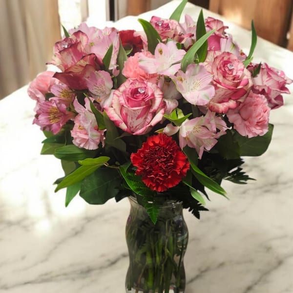 Pink roses and alstroemeria in a clear glass vase with a red carnation