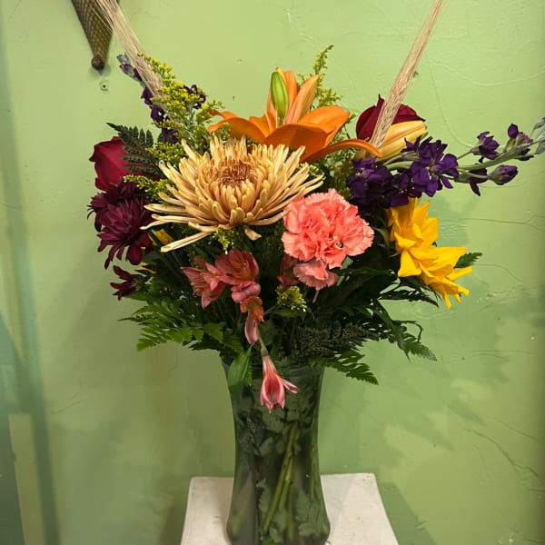 Mixed bouquet in a tall glass vase with orange, purple, yellow, and pink flowers