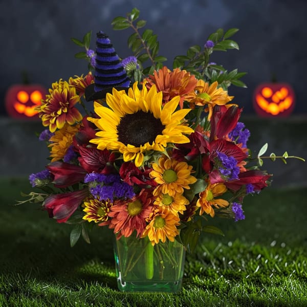 Colorful bouquet with sunflowers, mums, and purple accents in a glass vase