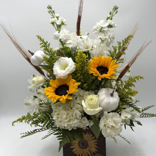 White floral arrangement with sunflowers in a dark vase and white pumpkins