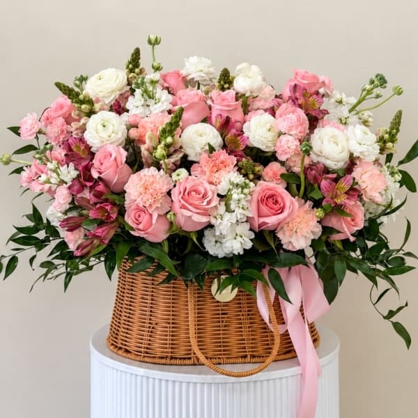 Pink and white flower arrangement in a wicker basket with a pink ribbon
