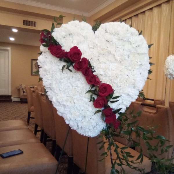 Heart-shaped white floral arrangement with red roses on an easel